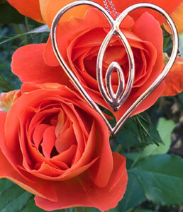 yoni Silver heart pendant with red flowers in the background